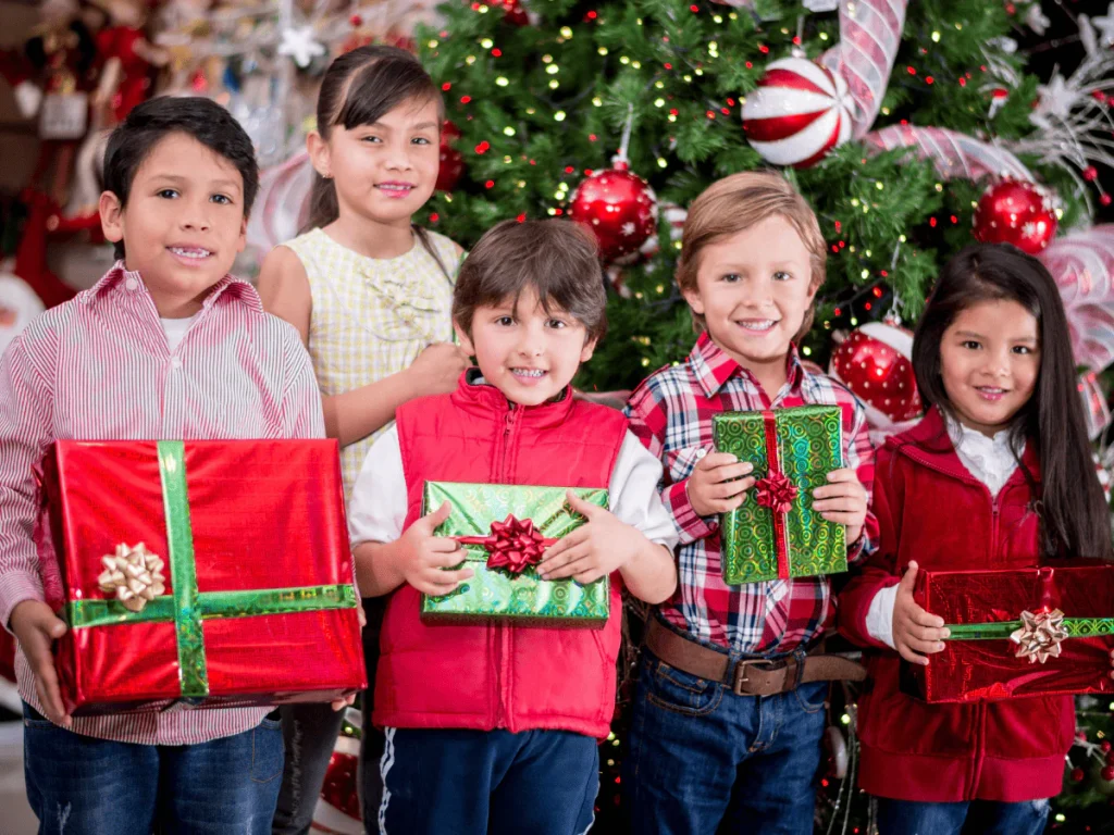 Kids opening cheap Christmas gifts with excitement under a decorated tree.