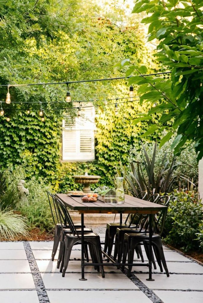 Backyard dining area with table and chairs on pavers instead of grass.