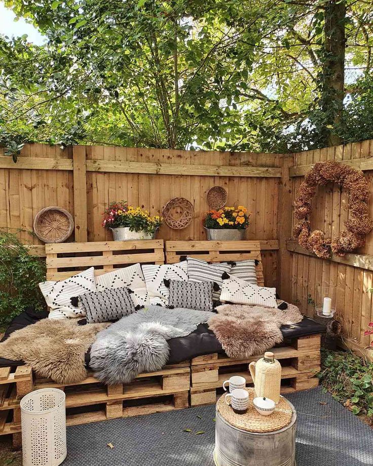 Backyard seating area made from wooden pallets with cushions on gravel ground.