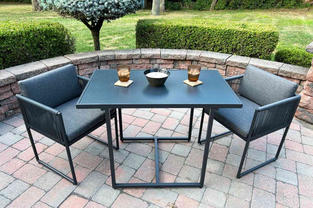 Compact metal patio table and chairs on paver backyard without grass.