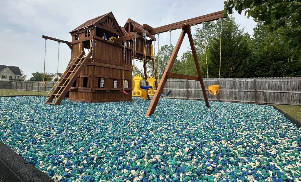 Backyard play area with rubber mulch and small play equipment instead of grass.