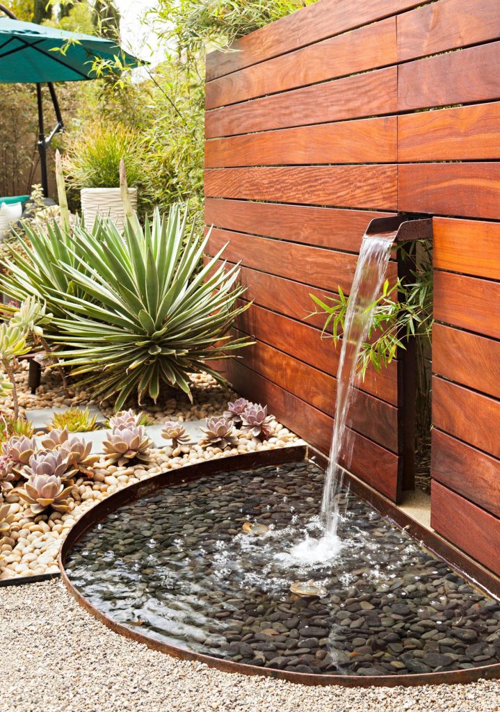 Small backyard fountain placed on gravel patio without grass.