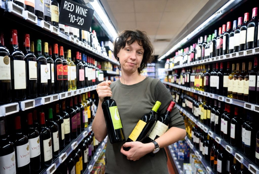 American shopper in wine aisle comparing best cheap red wines under 20 dollars in 2026.