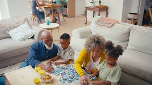 Multi-generational family grandparents parents and kids working together on a jigsaw puzzle at a living room coffee table, perfect example of relaxing cheap puzzles for family fun.