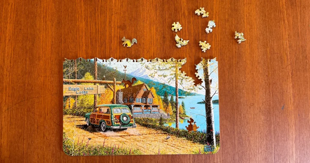 Partially completed scenic jigsaw puzzle on a wooden table showing a detailed landscape with cabin and lake, demonstrating satisfying results from affordable jigsaw puzzles.