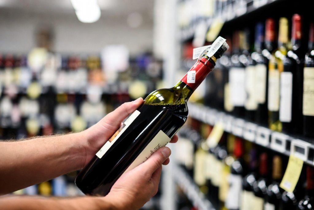 Shopper learning how to choose the best cheap red wine by reading labels in a US store.